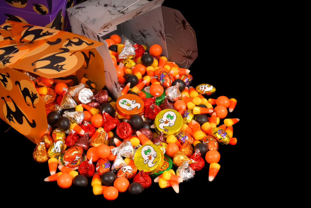 Image of three boxes with halloween pics toppled over with brown, orange, yellow, read candies spilled out including candy corns.